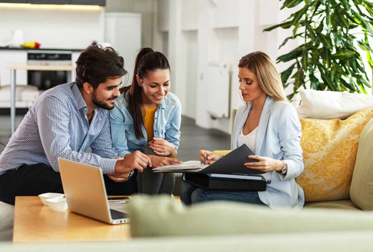 Homeowners review property documents with a real estate agent at a dining table.